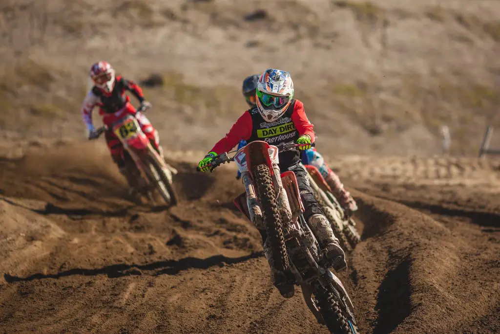 Three people riding motocross on sandy terrain