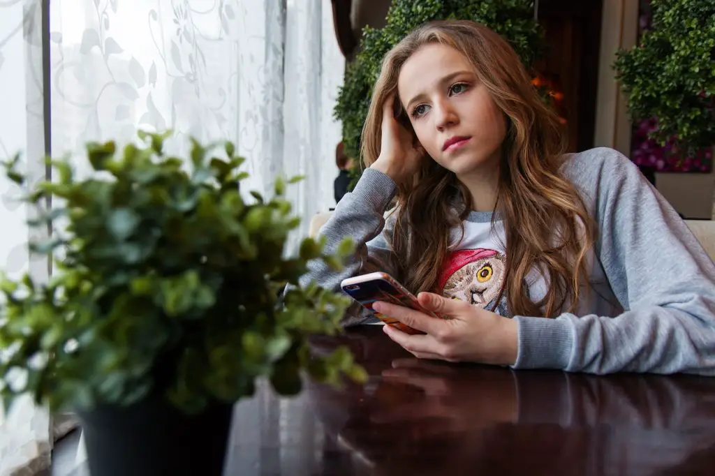 Woman with cell phone sits bored in restaurant - not a nice polterabend mistake