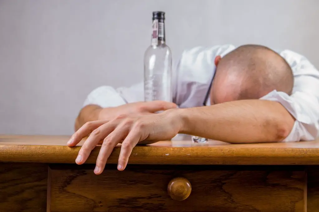 Mann mit Vodkaflasche liegt schlafend auf einem Tisch - ein Kater als einer der größten Polterfehler