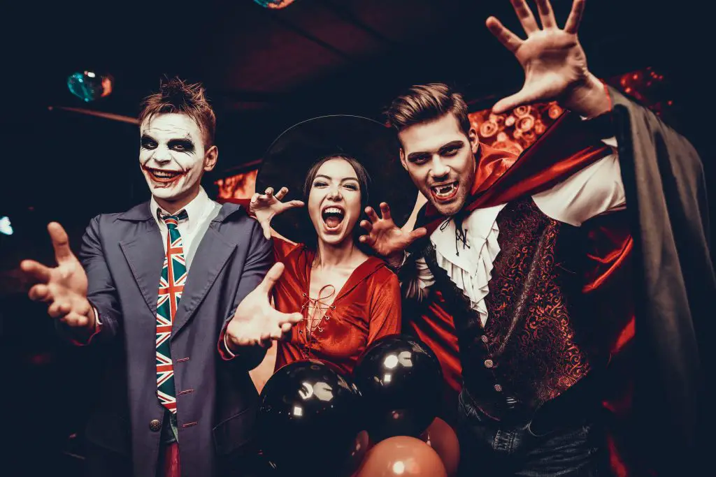 Man in zombie costume, woman in witch costume and man in vampire costume have costume party